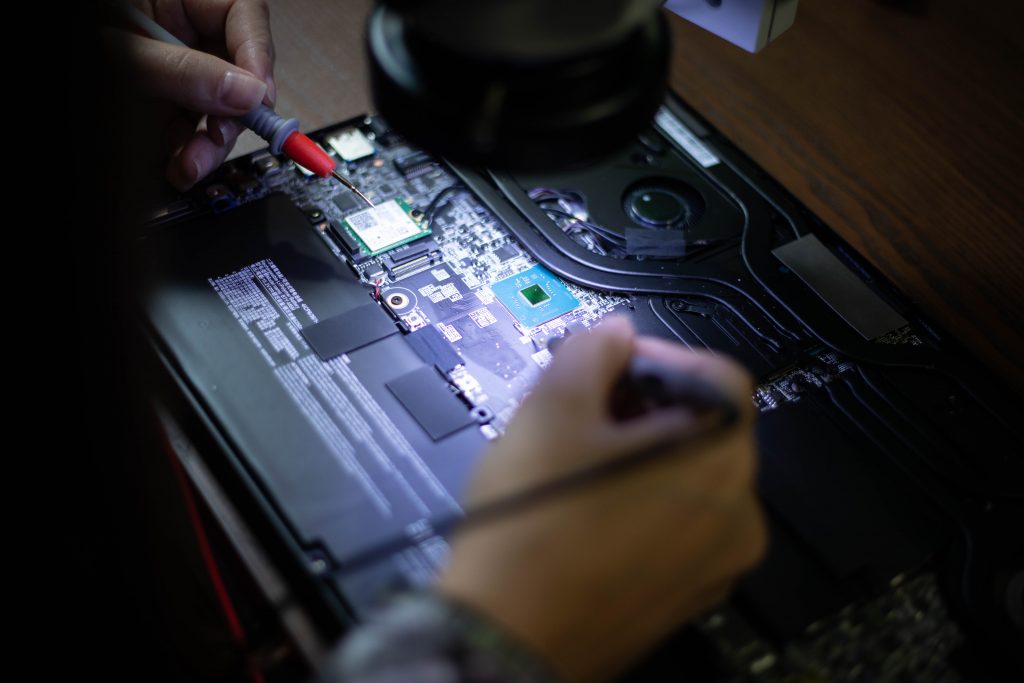 Probing a gaming laptop motherboard with a multimeter during fault diagnosis
